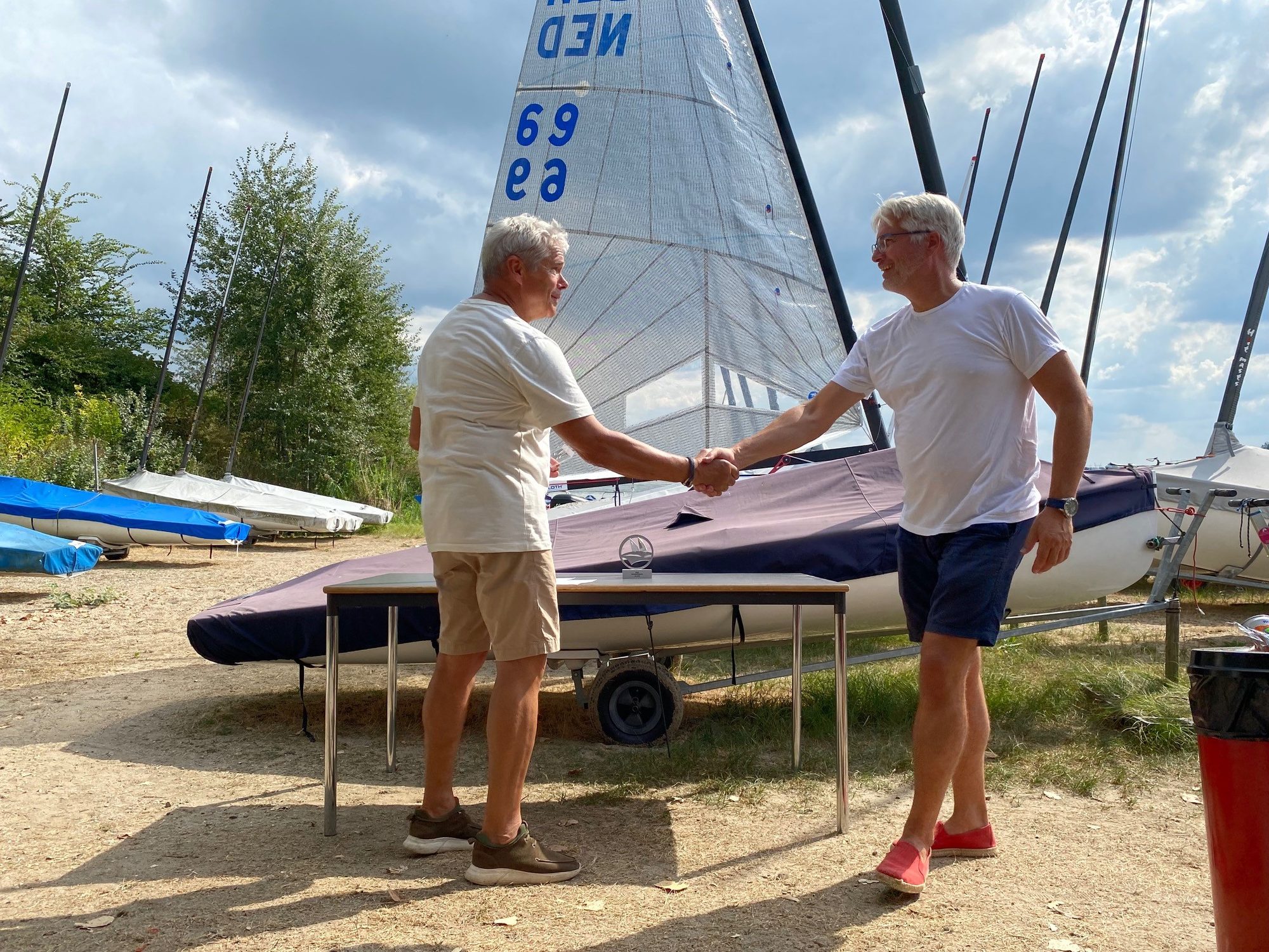 Twee clubleden schudden elkaar de hand op het strand bij de club